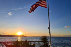 Hier sieht man eine USA Flagge am Meer, während gerade die Sonne untergeht.